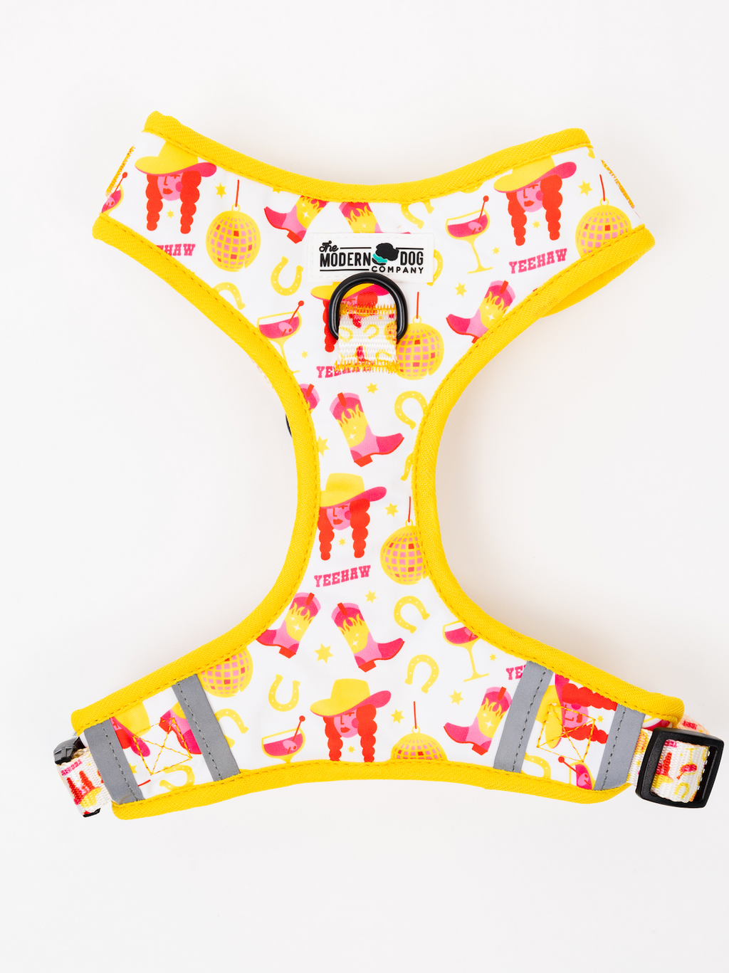 A white dog harness with a bright yellow border and a colorful western-themed print featuring pink boots, yellow hats, horseshoes, and the words 'YEEHWAW'. The harness has reflective gray stripes and a black metal ring.