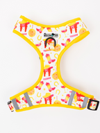 A white dog harness with a bright yellow border and a colorful western-themed print featuring pink boots, yellow hats, horseshoes, and the words 'YEEHWAW'. The harness has reflective gray stripes and a black metal ring.